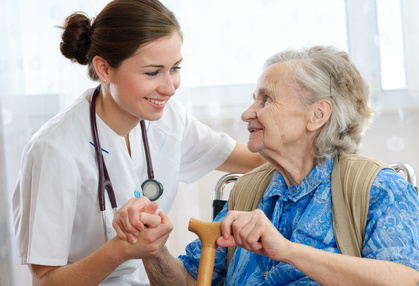 krankenpflegerin und alte Frau im Rollstuhl halten sich an der Hand und lächeln sich an